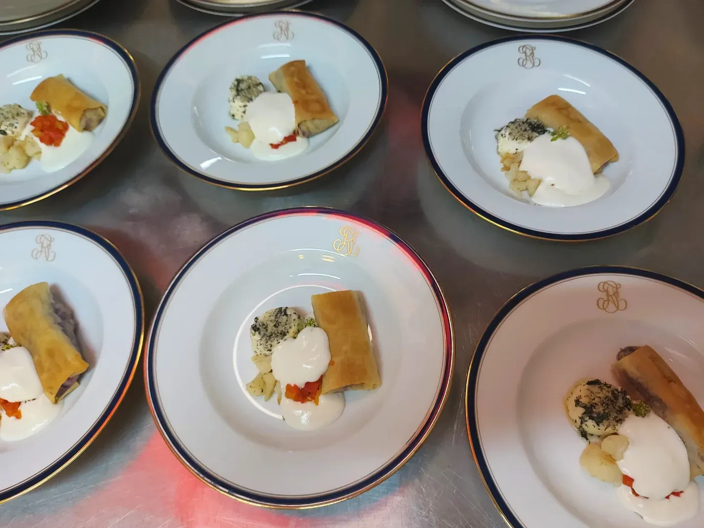 Six plates with a golden spring roll, herb cheese and white sauce on china with a navy rim