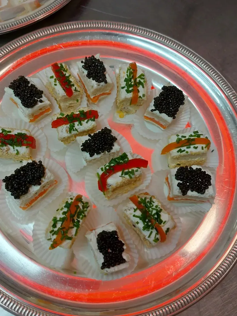 Silver tray of canapés topped with black caviar, chives and roasted pepper