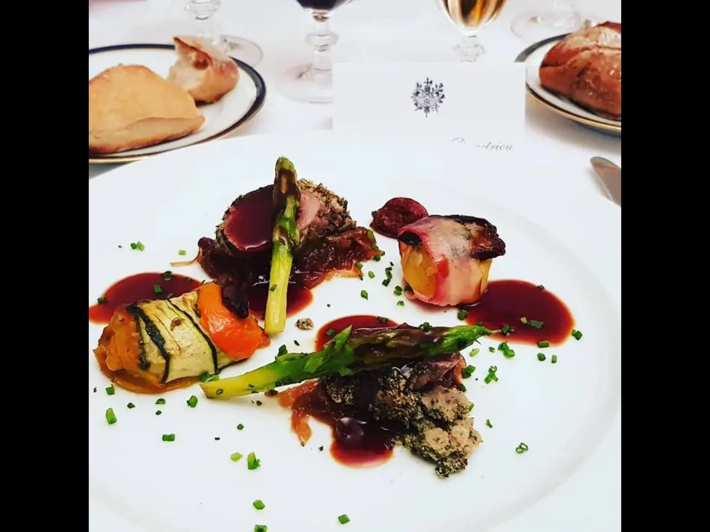 A plated main with a herb-crusted fillet, asparagus, a courgette roll and red wine sauce