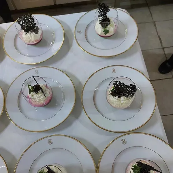 Rows of glass desserts topped with a black tuile on gold-rimmed plates