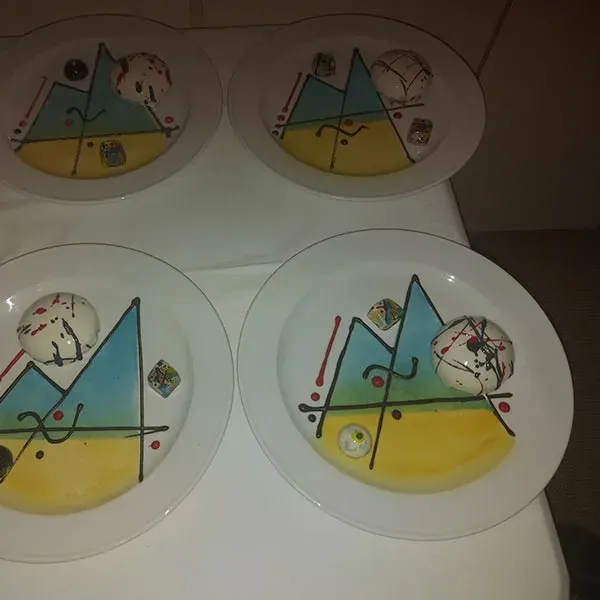 Four white plates painted in blue and yellow with a white dessert dome
