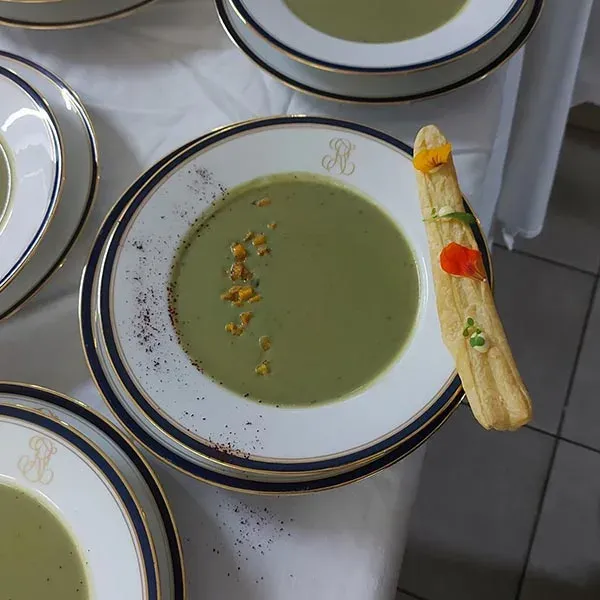 Green soup with a puff pastry stick and edible flowers on monogrammed china