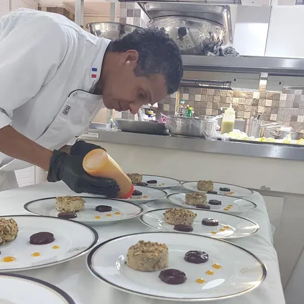 Dominique plating a dessert sauce onto rows of plates in a professional kitchen