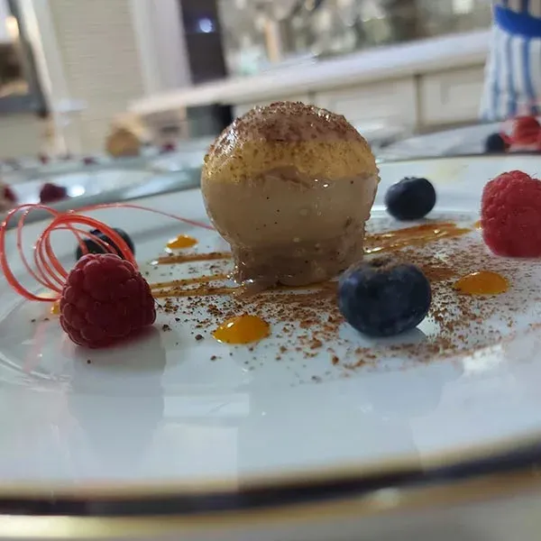 A chocolate dome dessert with raspberries, blueberries and a red sugar spiral